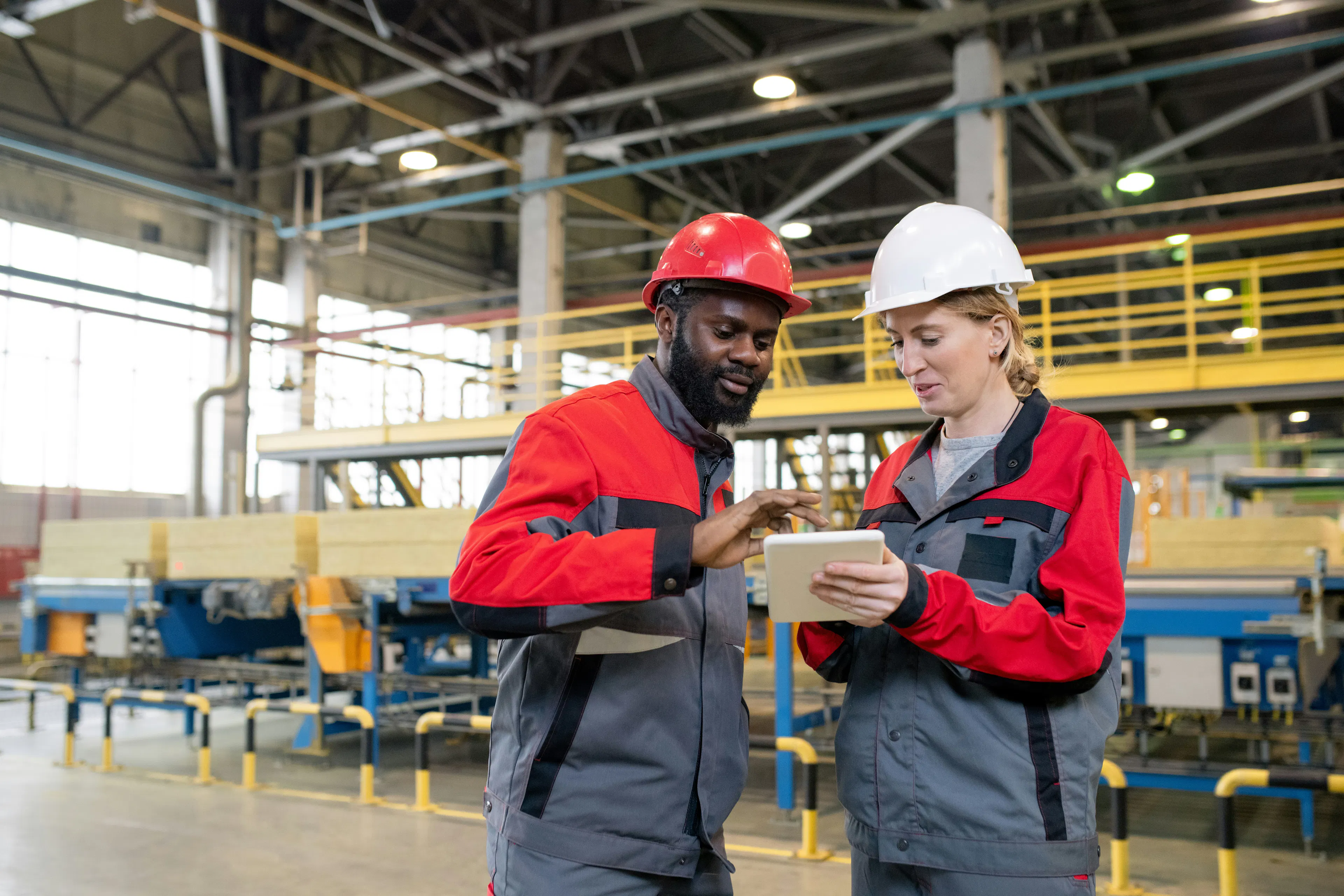 Two shift workers in hard hats reviewing tablet