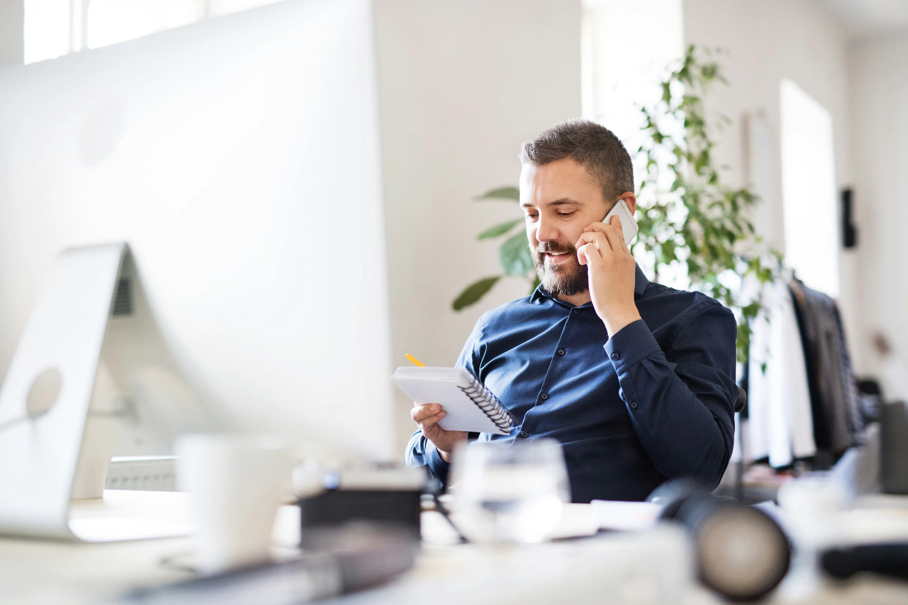 Man on phone holding notepad at office desk