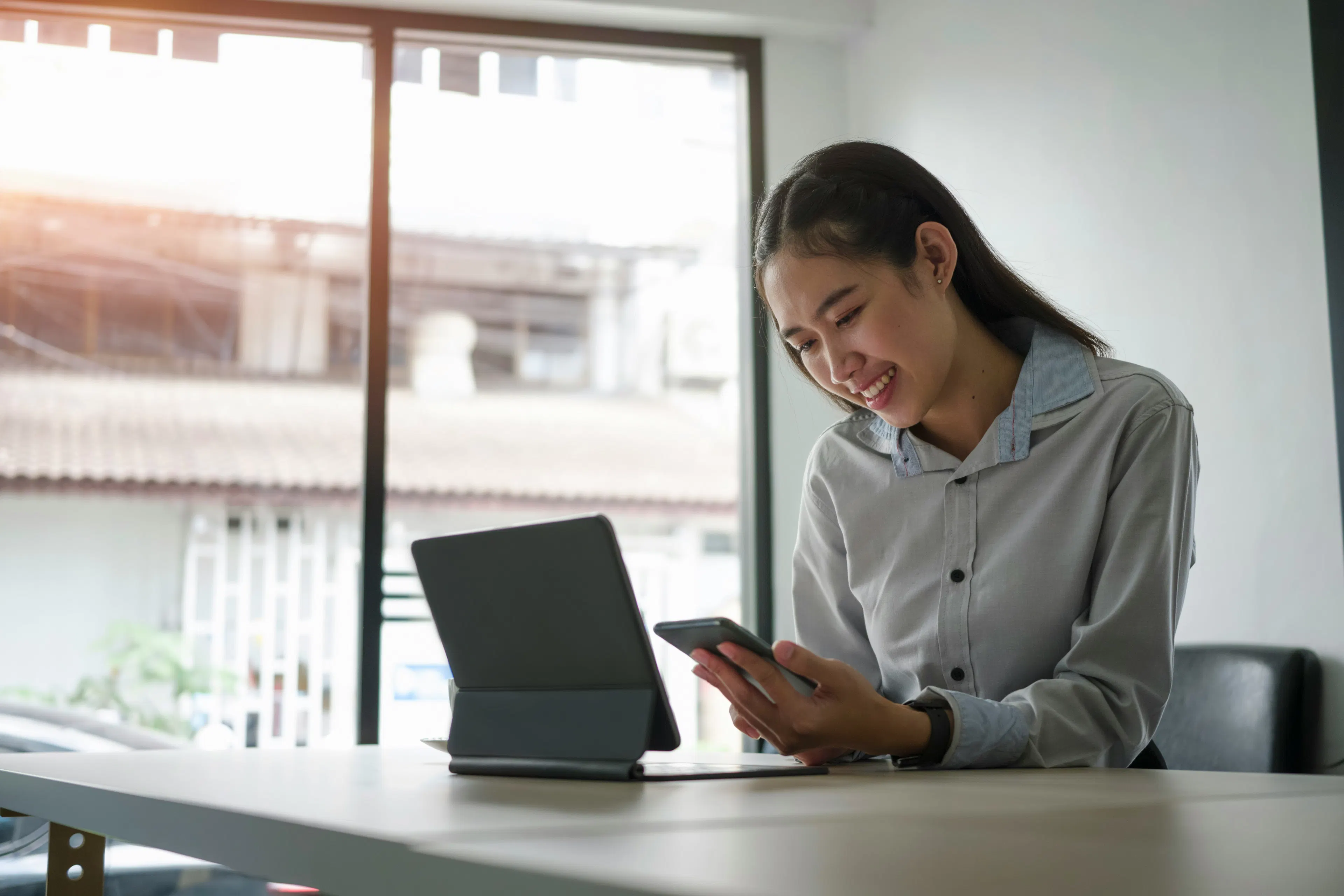 Woman smiling at phone with tablet on desk