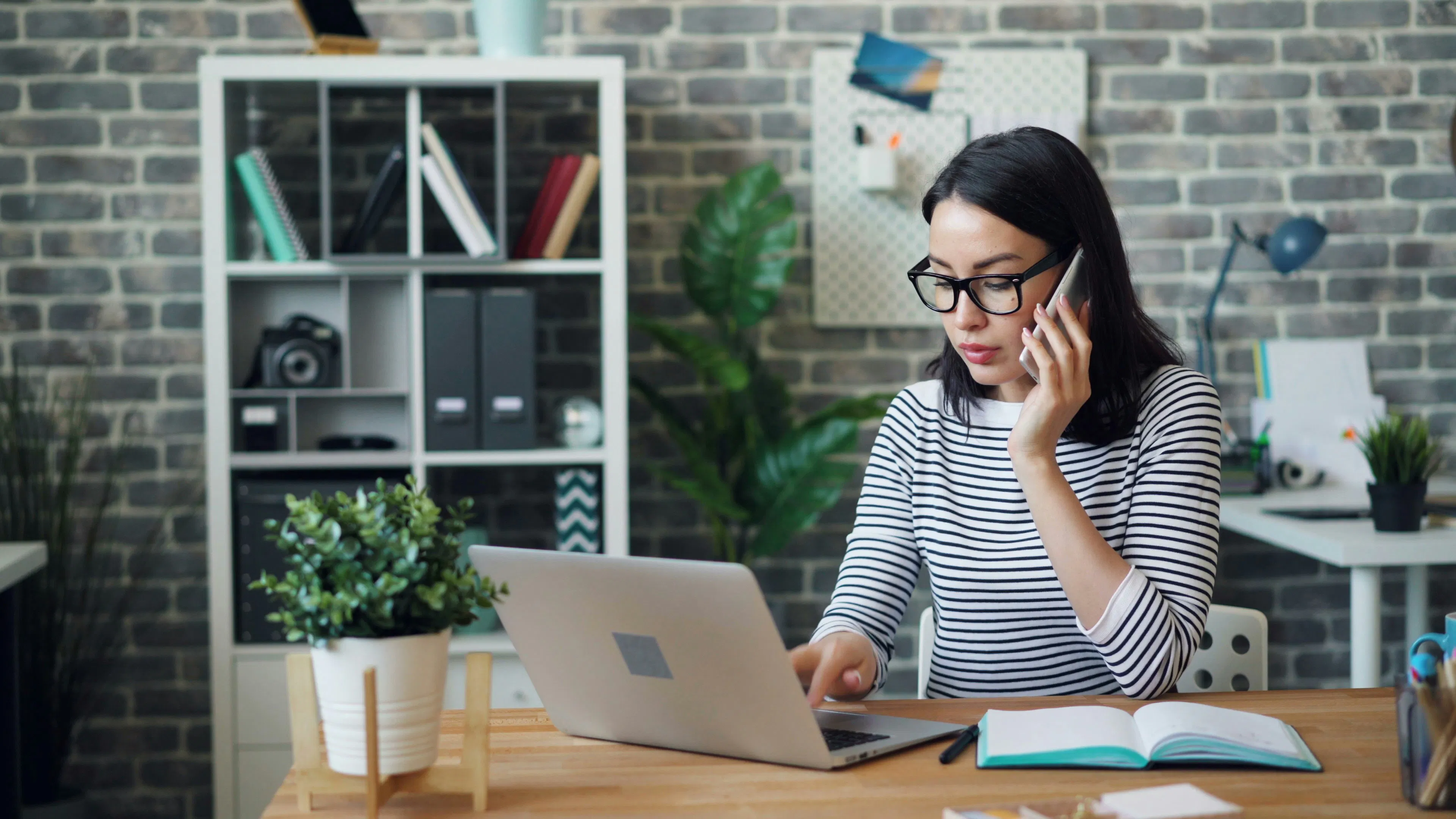 Woman talking on phone while using laptop at office desk
