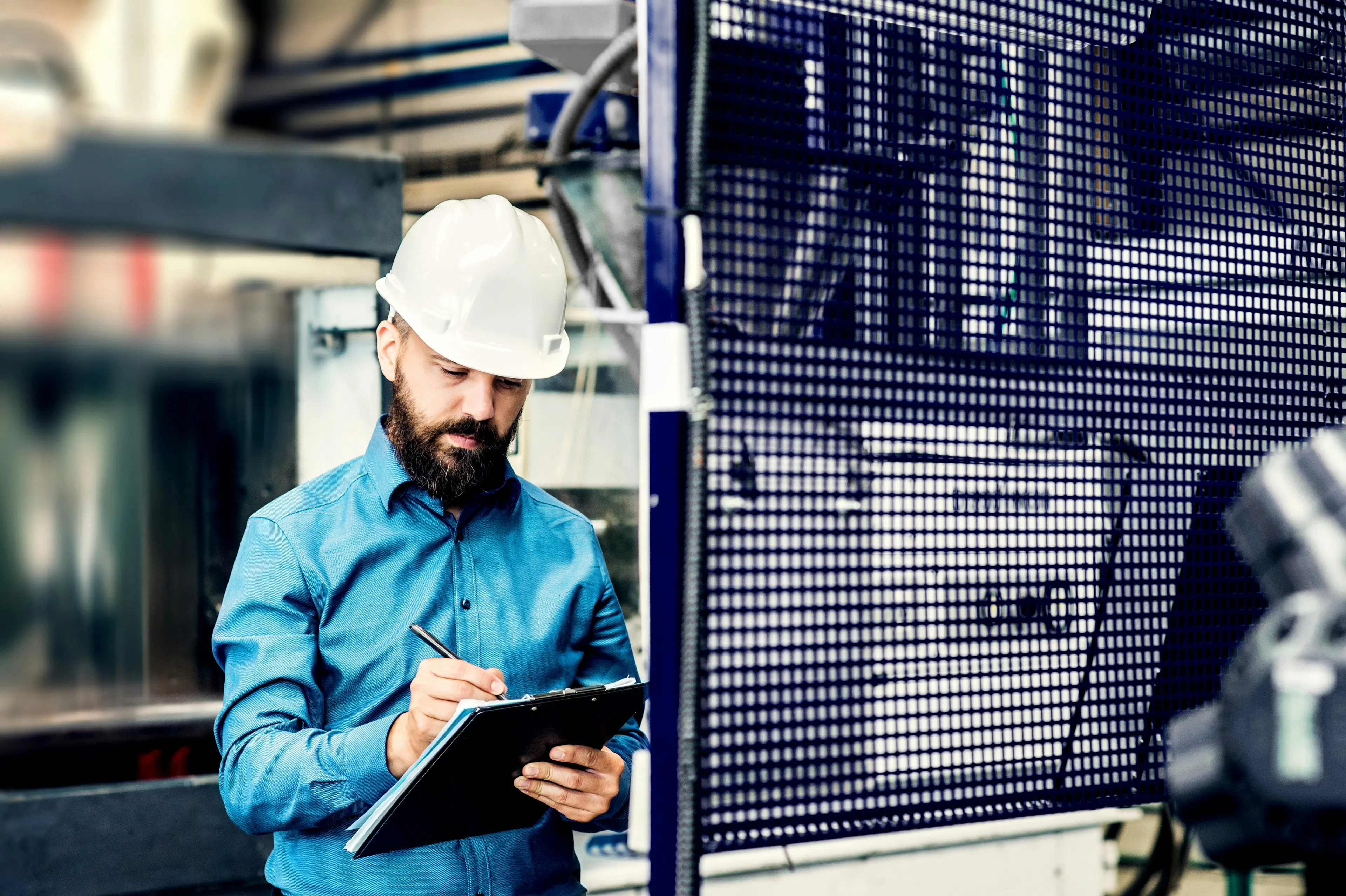 Industrial worker in hard hat writing notes on clipboard