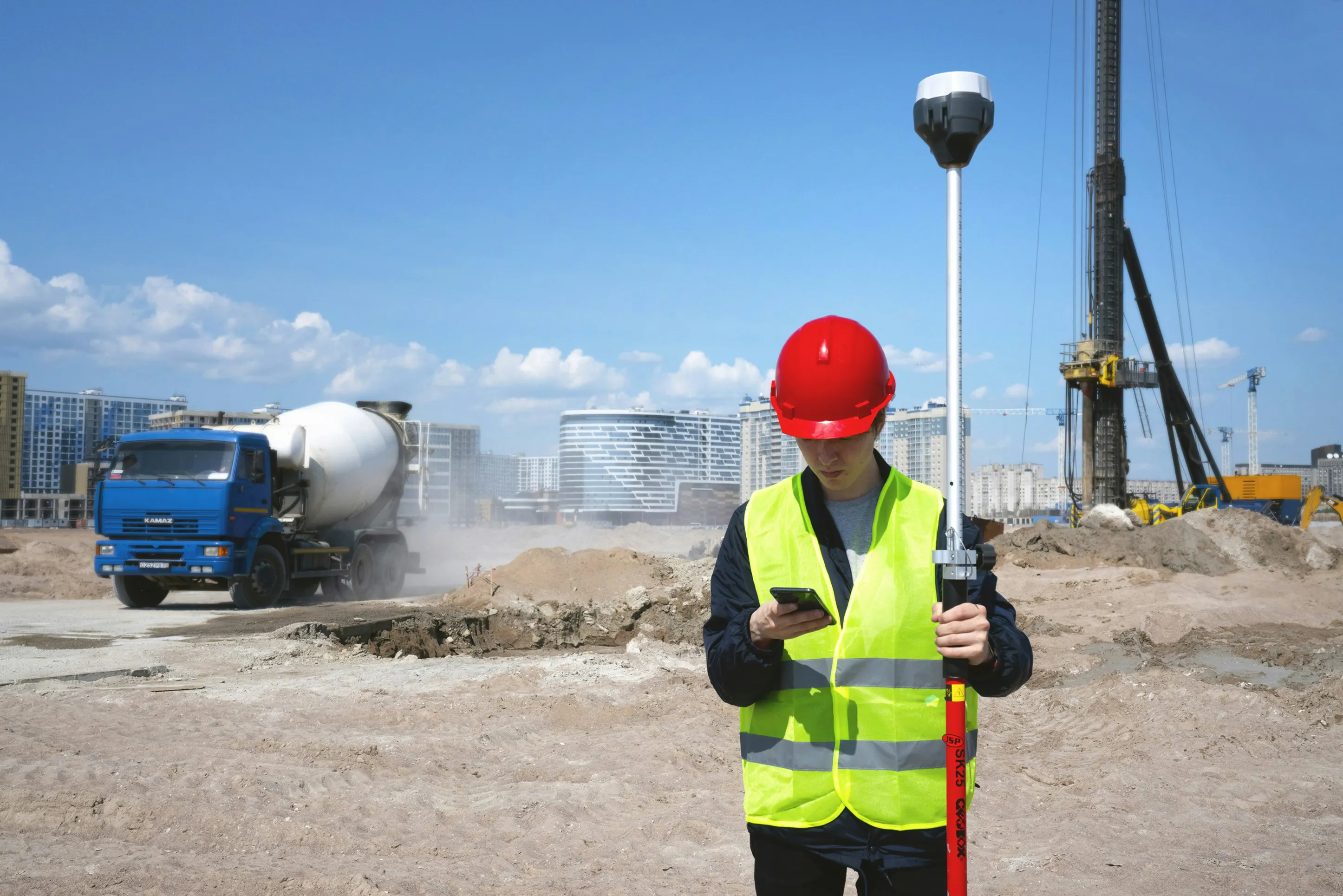 Construction worker in red hard hat and yellow safety vest reading message on smartphone at construction site