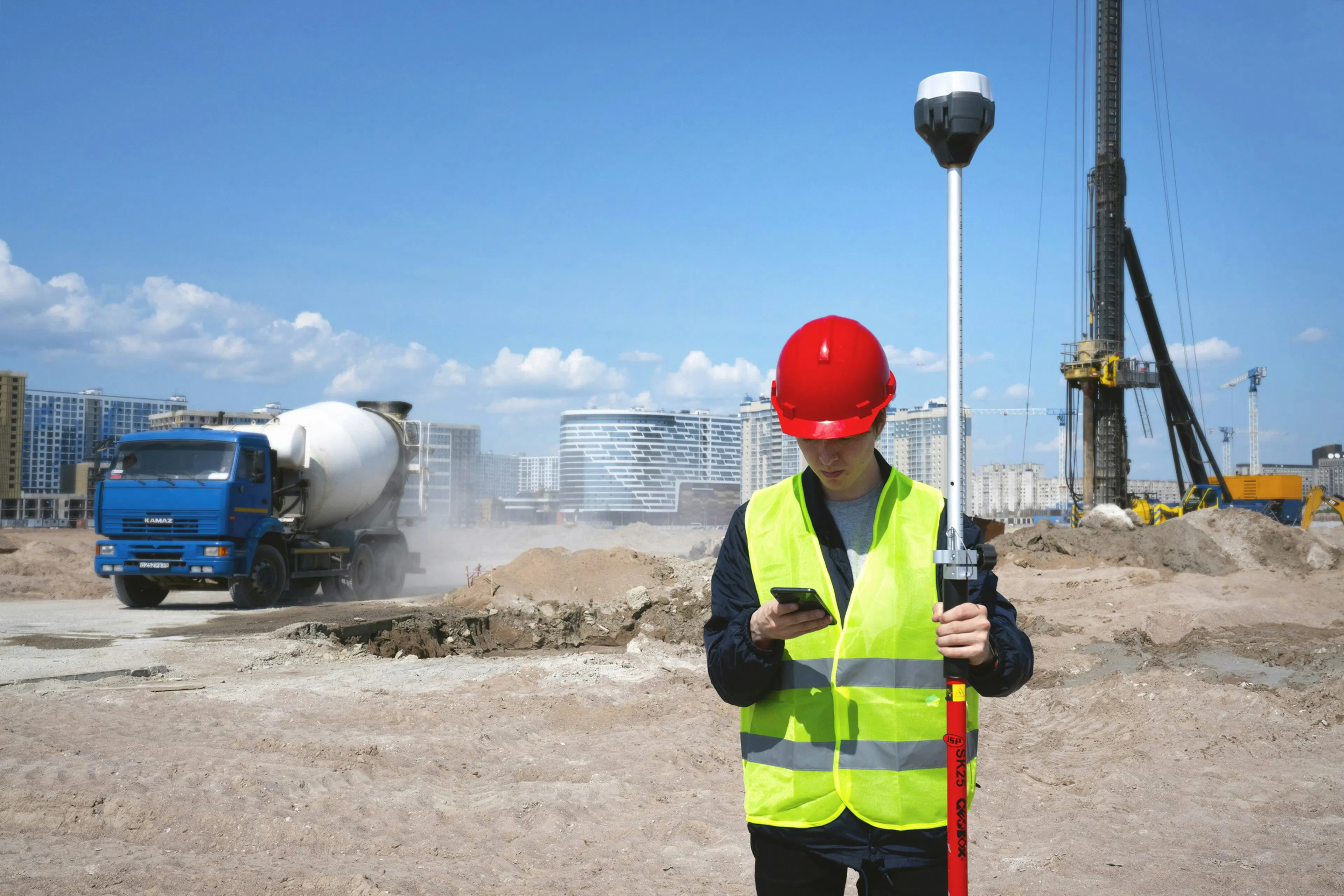 Construction worker in red hard hat and yellow safety vest reading message on smartphone at construction site