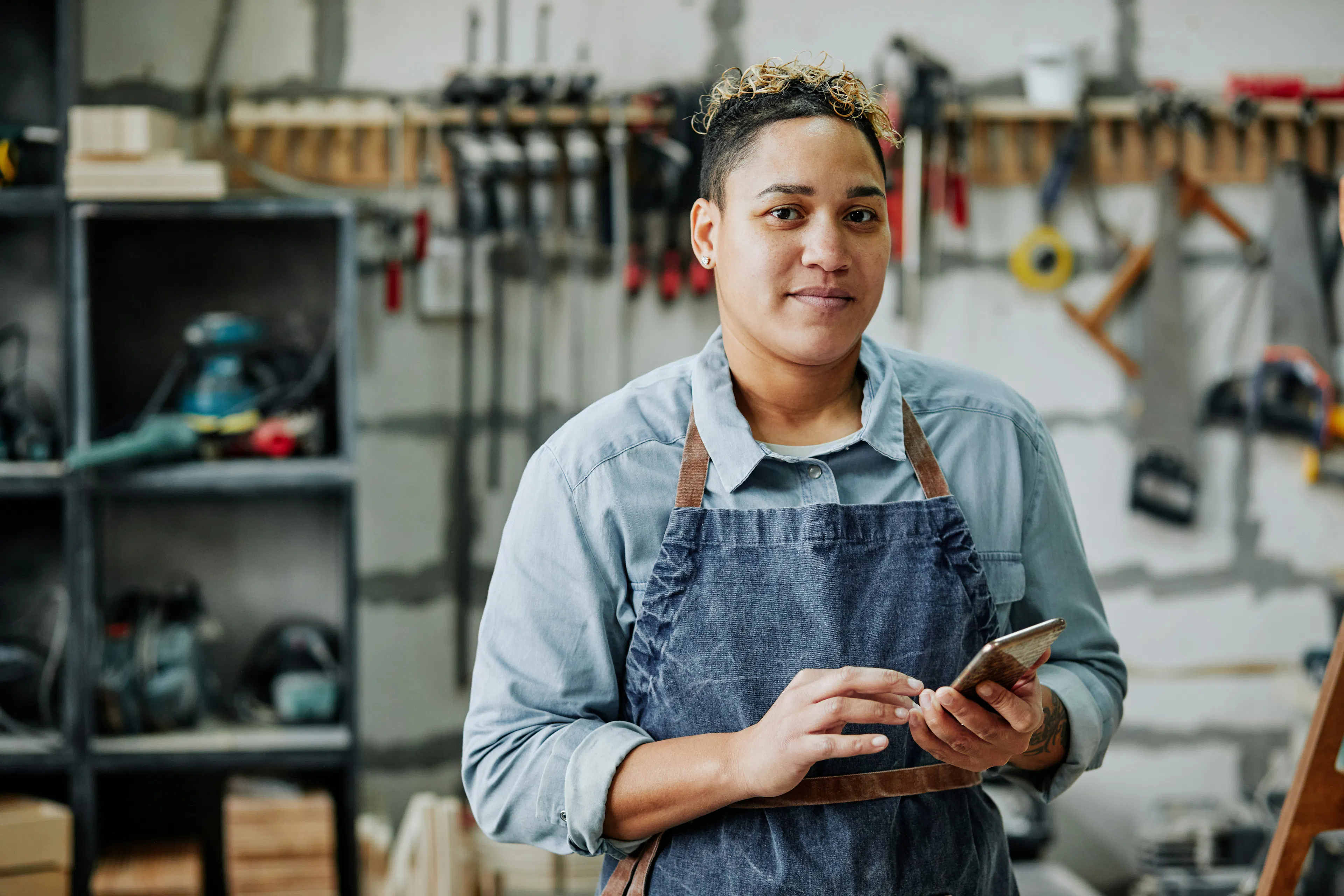 Worker in a denim apron holding a smartphone in a workshop
