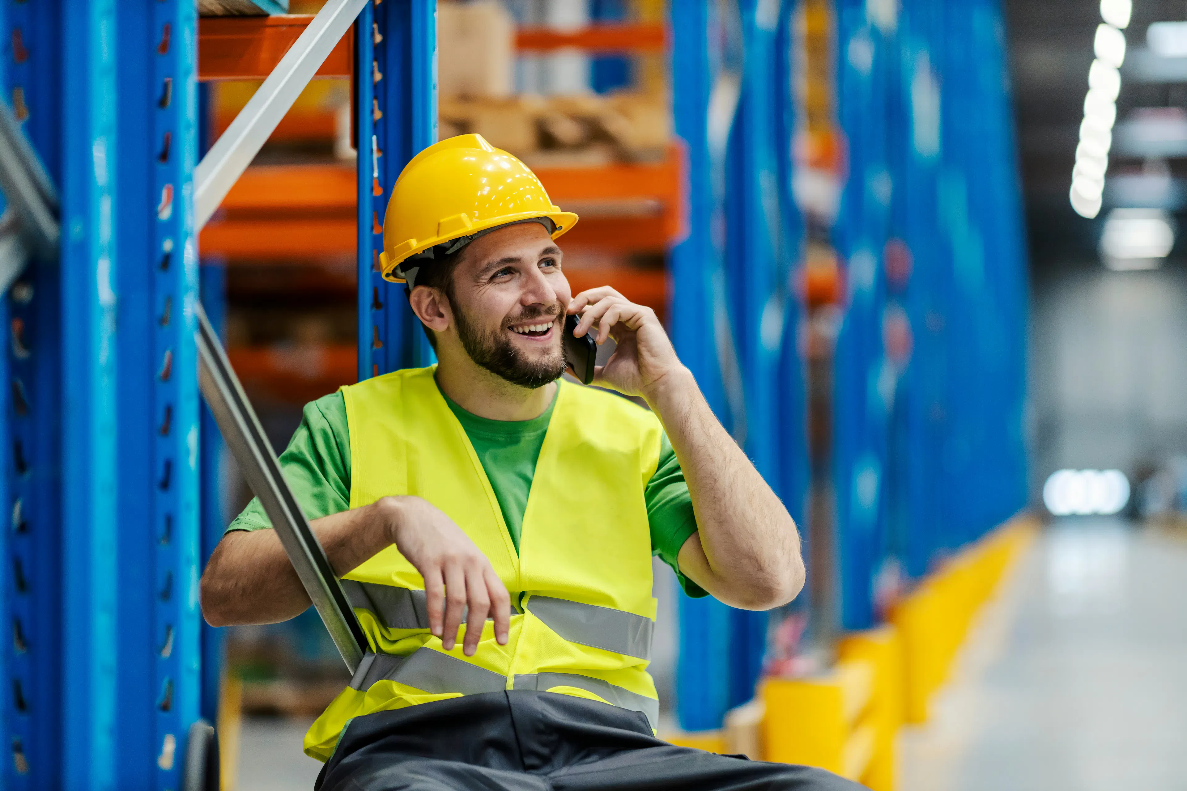 Smiling warehouse worker in a hard hat talking on a phone
