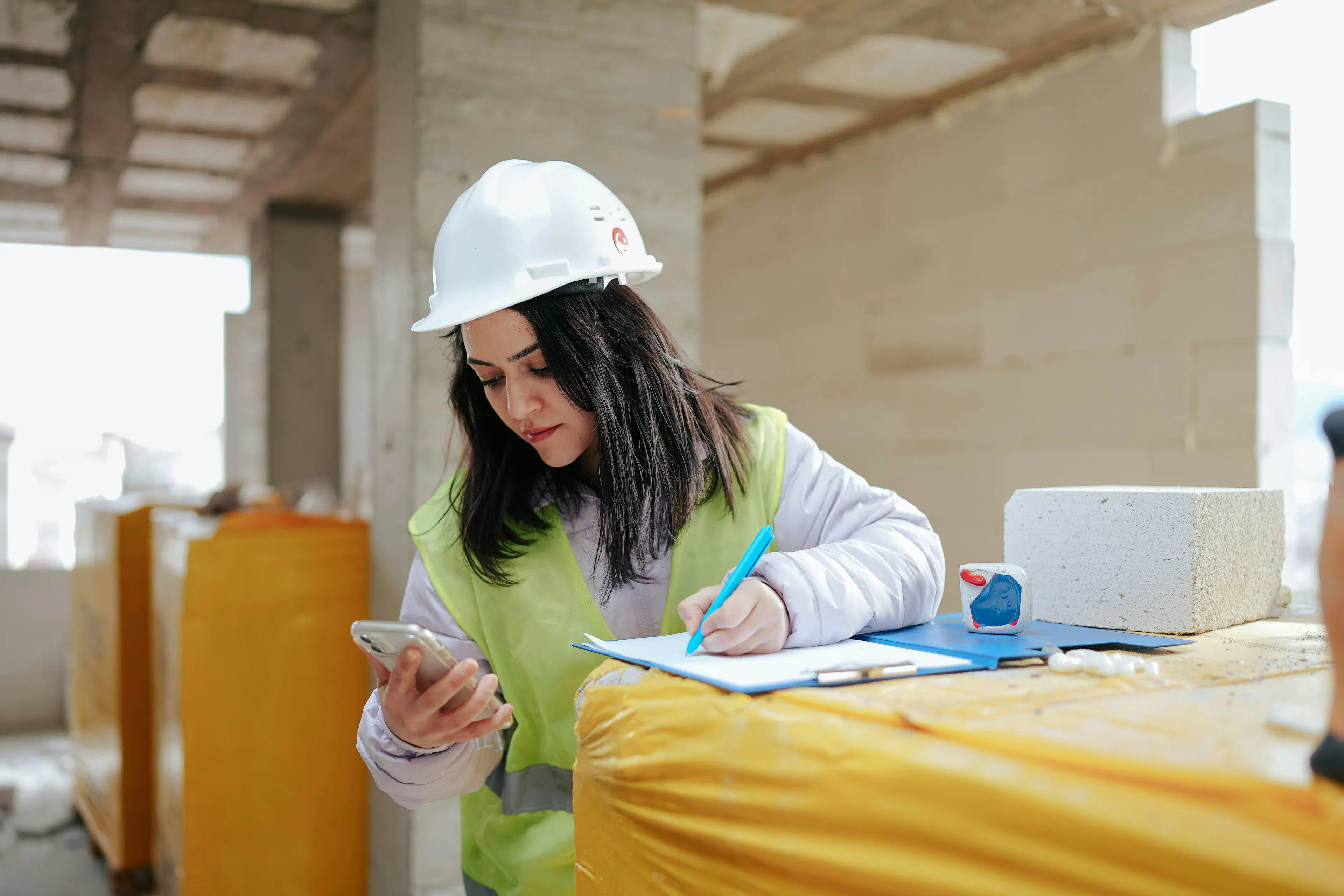 Construction worker recording safety data on clipboard with phone
