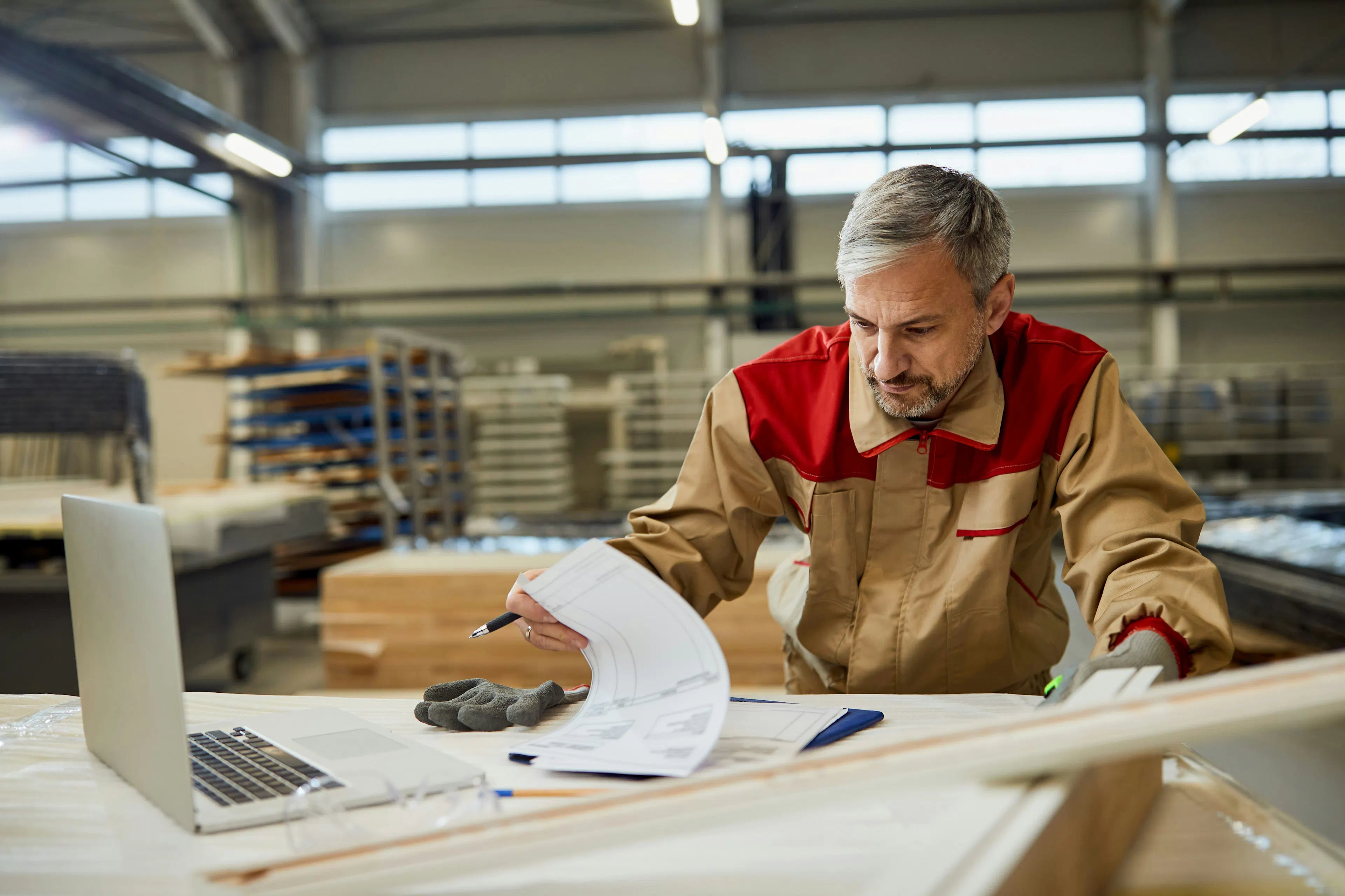 Worker reviewing documents at a bench on a factory floor.