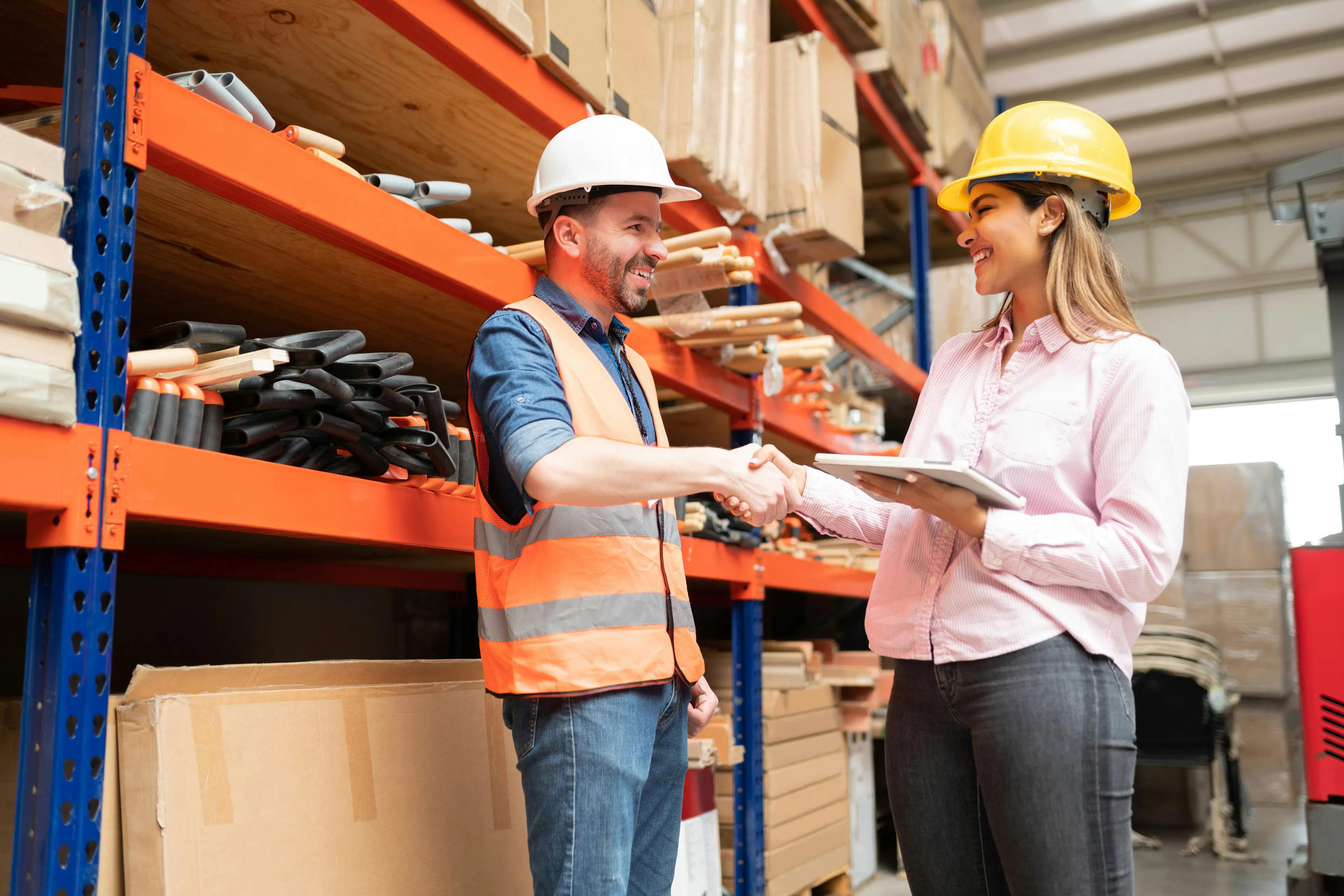 Warehouse worker in a hard hat shaking hands with a manager.
