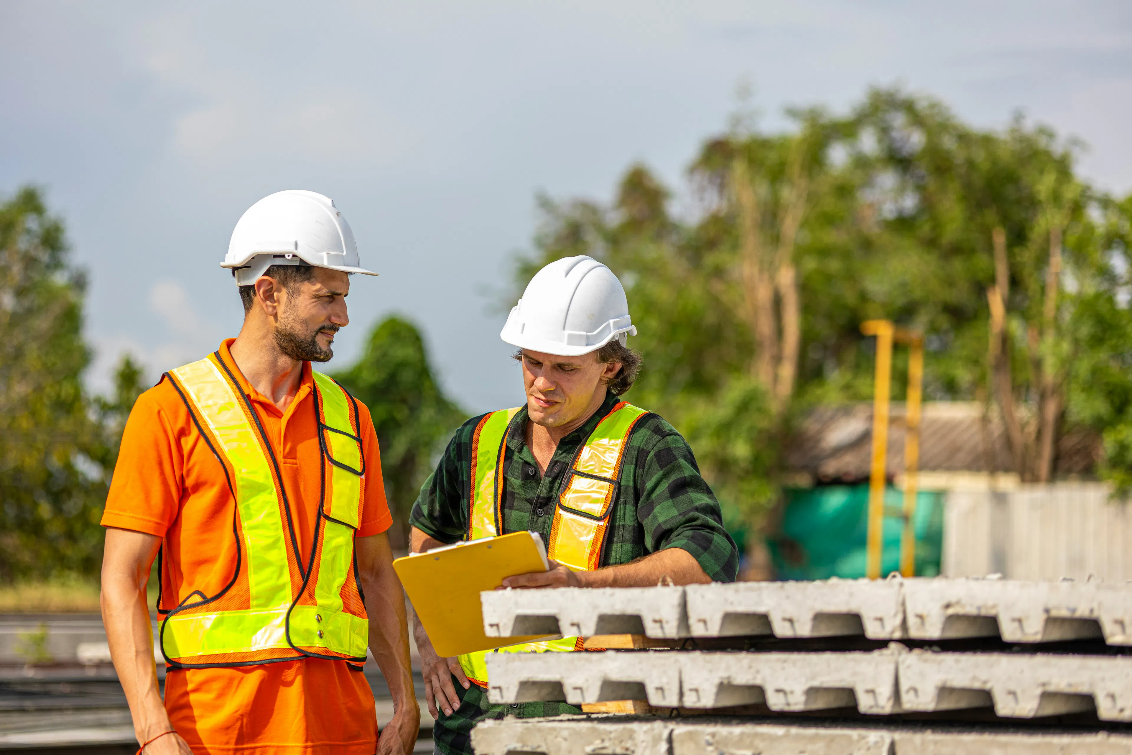 Two construction workers in hard hats reviewing a clipboard together