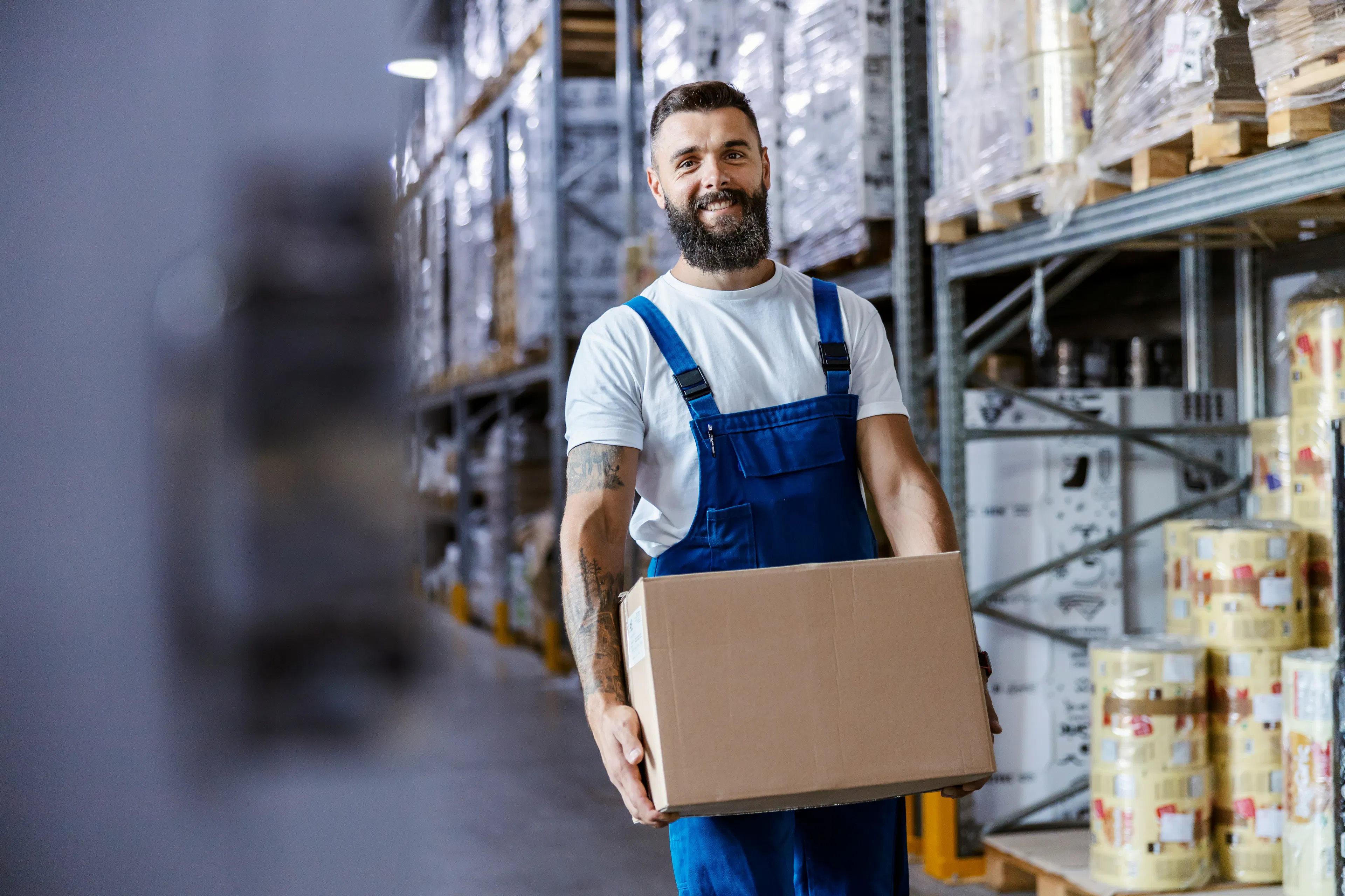 Warehouse worker in overalls carrying a cardboard box