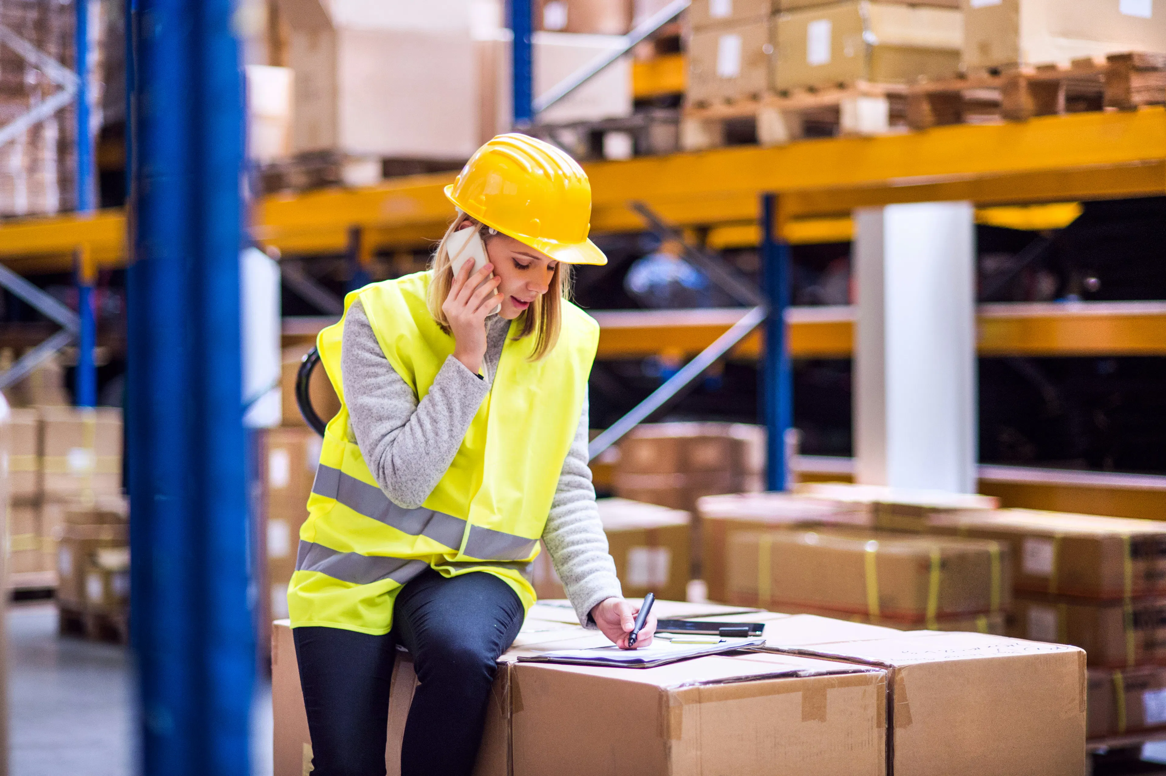 Warehouse worker on phone while writing on paperwork
