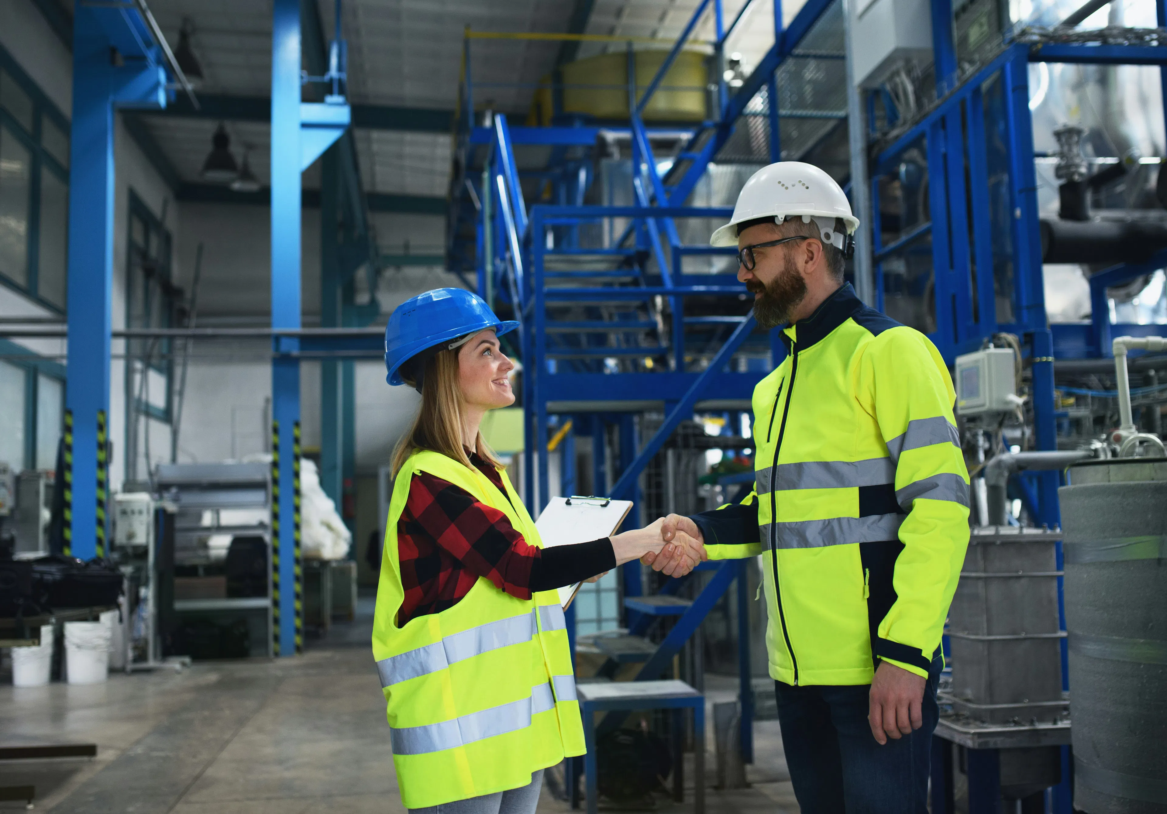 Two workers in hi-vis vests shaking hands on a plant floor.
