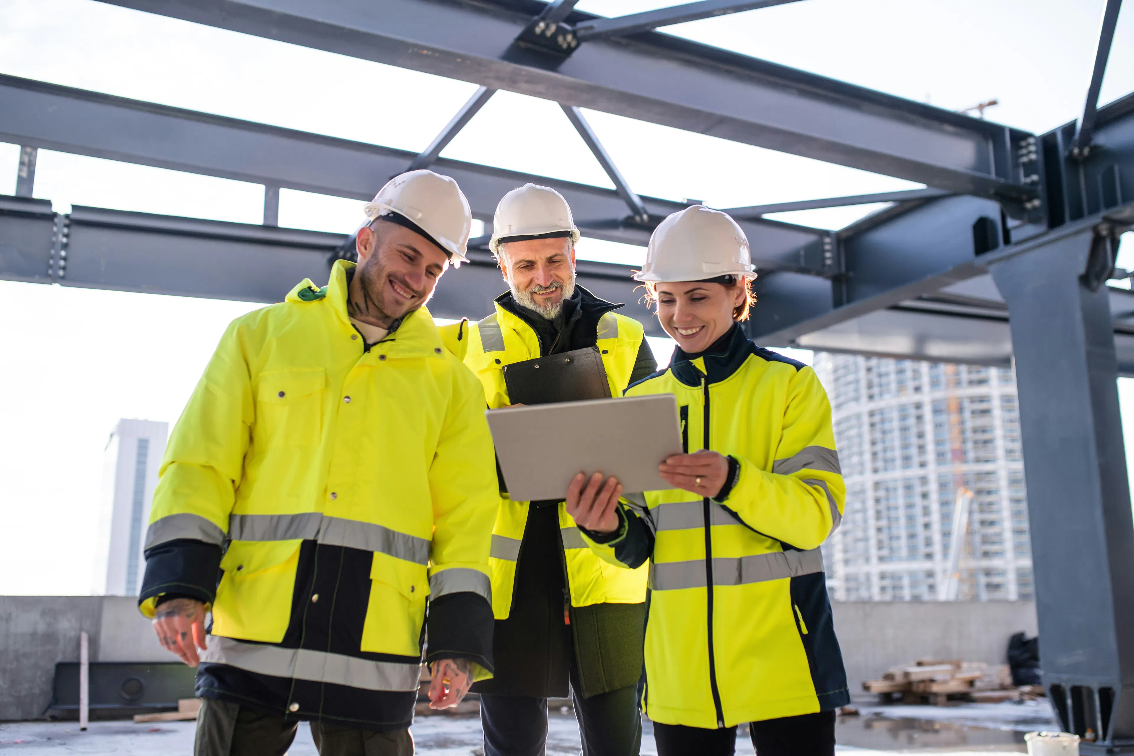 Three workers in hi-vis around a tablet, steel frame behind.
