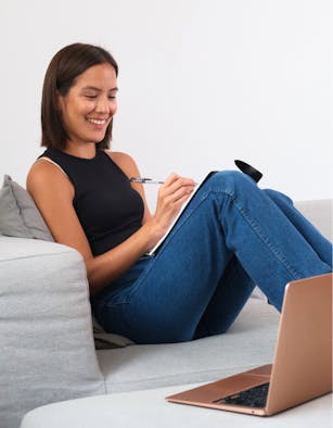 Photo of a smiling Indigenous teen girl writing in her notebook with her laptop open beside her, photo by Supernaturals Modelling