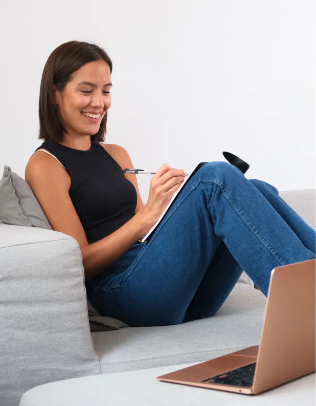 Photo of a smiling Indigenous teen girl writing in her notebook with her laptop open beside her, photo by Supernaturals Modelling