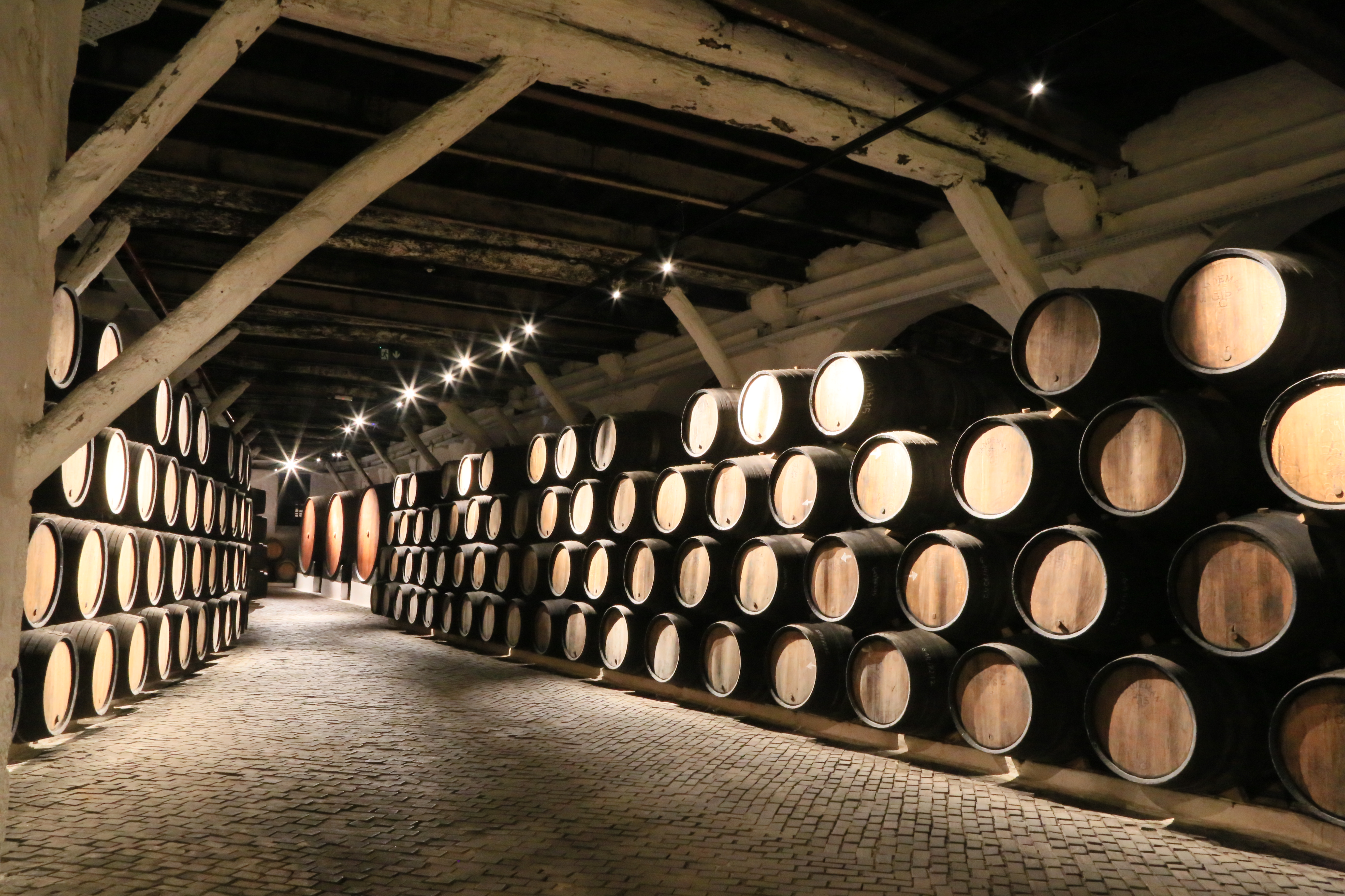 Stacked barrels 4 rows high sit in the cave at a winery and are well-lit by ceiling lights. Portugal. There are no people in this photo.