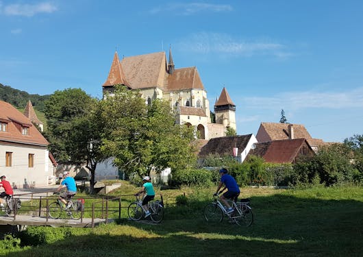 A group of 6 adult bikers cycle over a bridge and into a charming Romanian town.