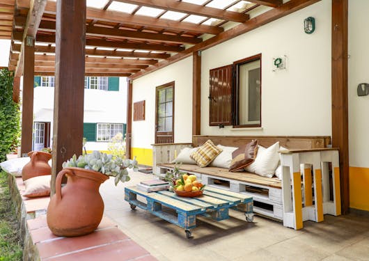 The patio outside one of the accommodations buildings for the Portugal Yoga Retreat is shown, with slatted coffee tables and benches, pottery vases with succulents in them, and brightly colored green and yellow accent paint.
