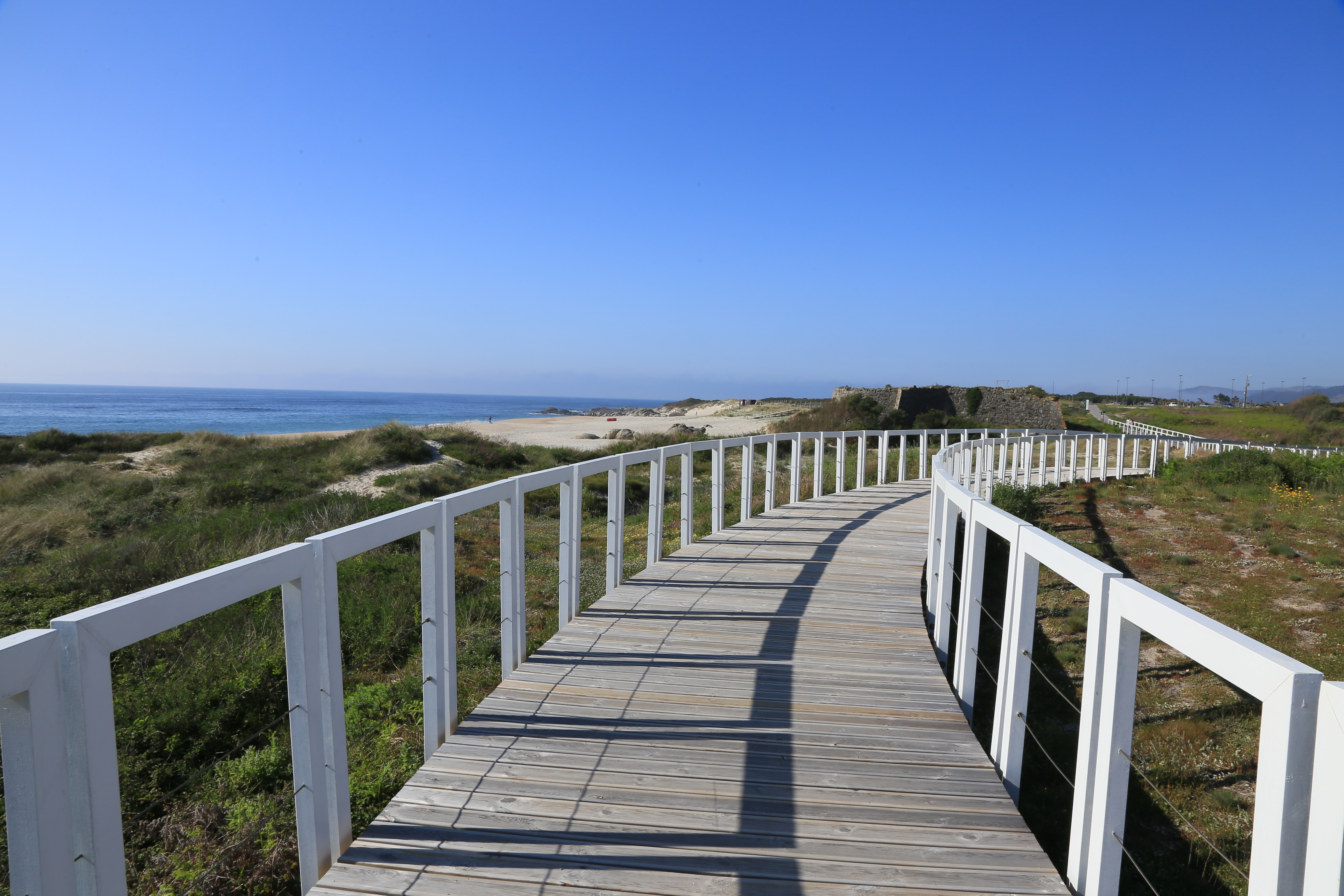 A wooden-slat boardwalk with freshly painted white railings on either side winds around the Atlantic Coast off Portugal.