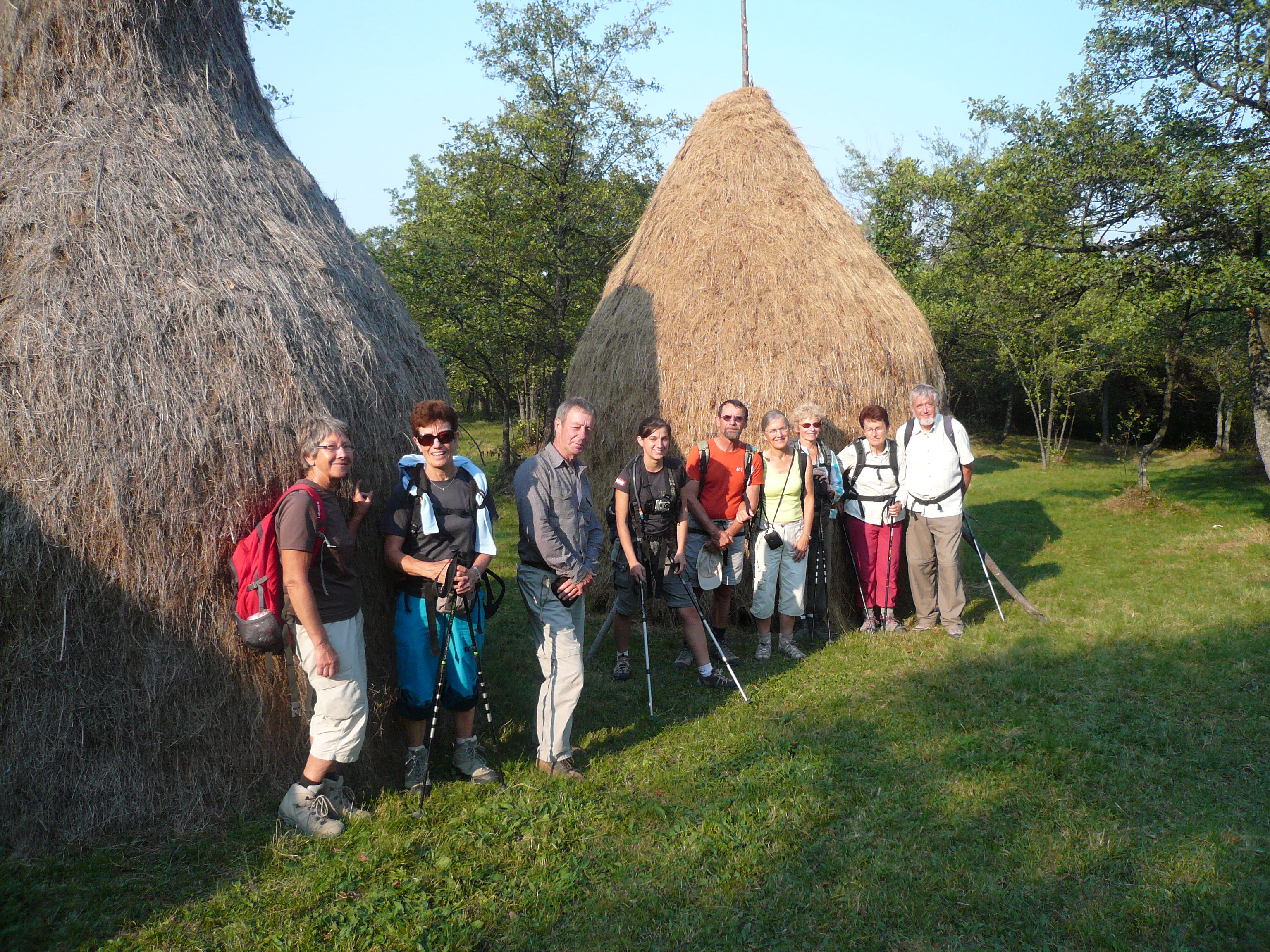 A group of 9 adult Caucasian hikers stand in front of two large haybales in Maramures Romania.