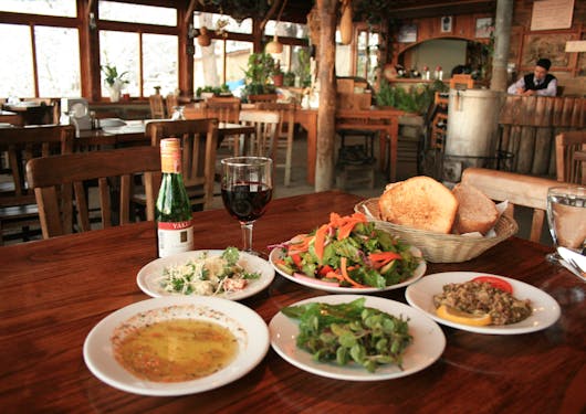5 plates of traditional cuisine with a glass of wine and a bread basket sit on a restaurant table in Western Turkey on the Slow Travel Food & Wine Tour.