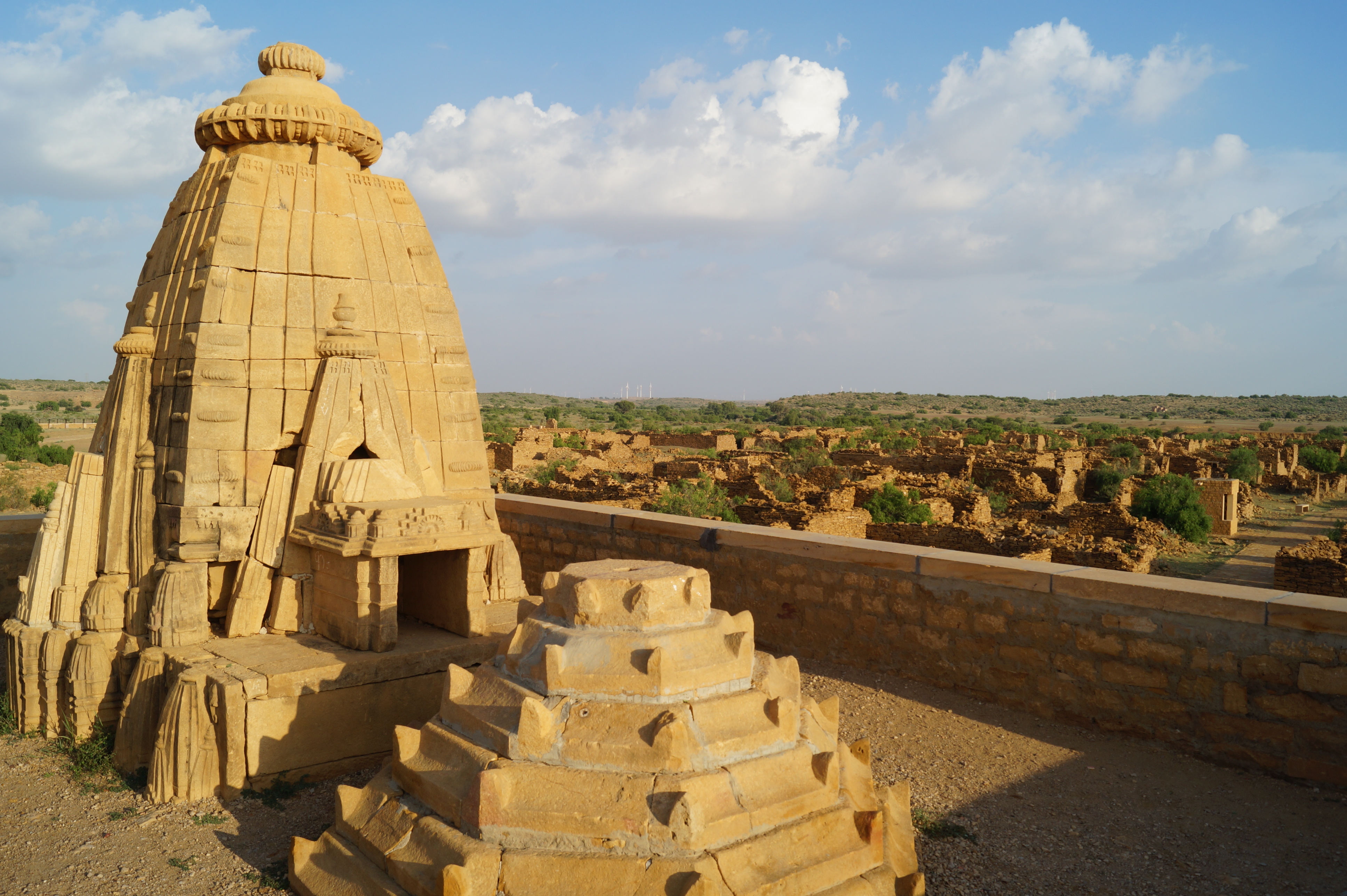 The Kuldhara Temple in Rajasthan is show at sunset with interesting formations in the center and left of the screen, and what looks like ancient ruins in the backdrop.