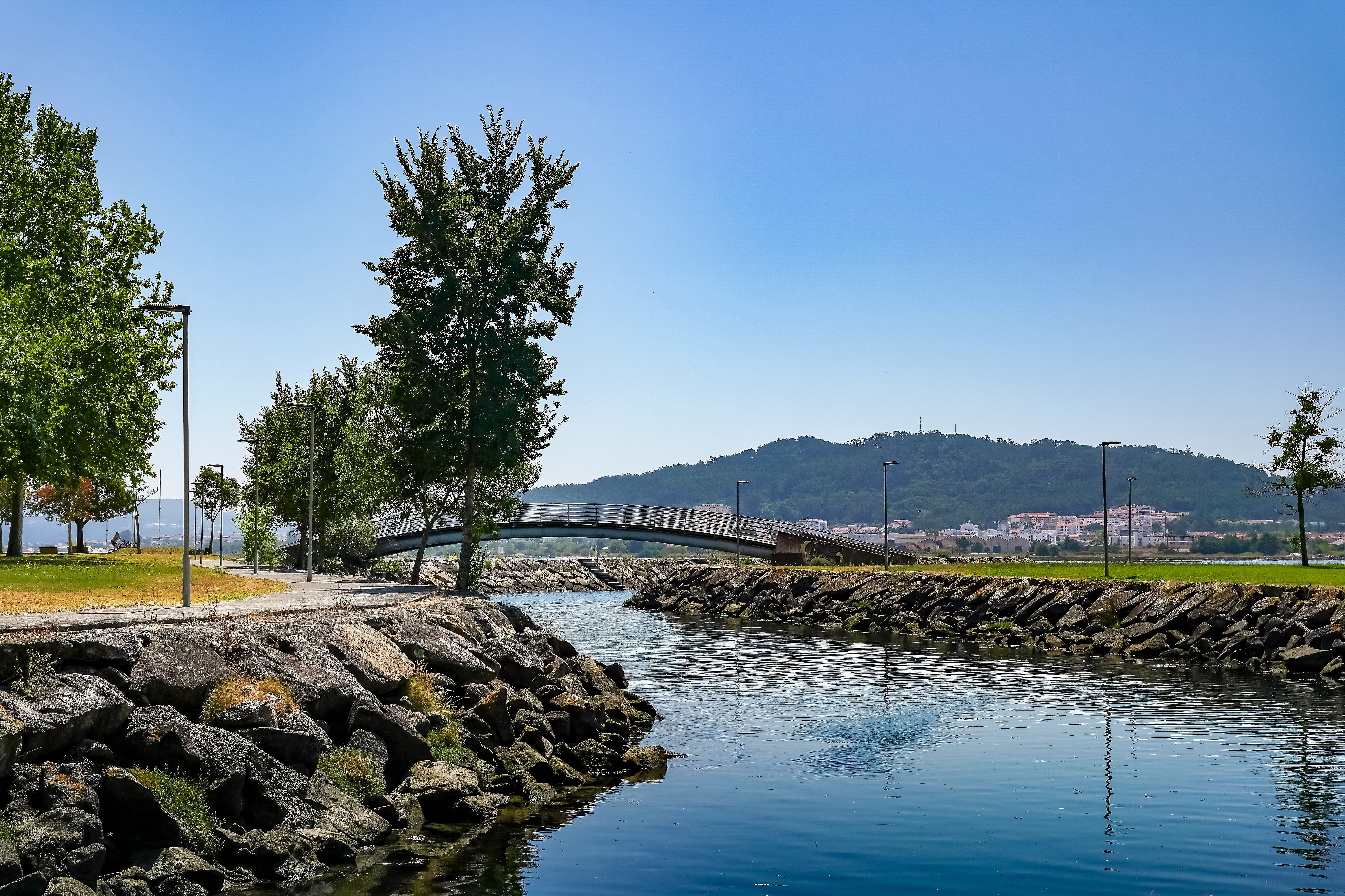 An arc-shaped bridge spans a flowing dark blue river. The banks are rocky on both sides and the sky is blue. This is in Portugal's Alto Minho region.