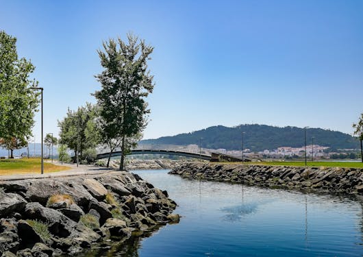 An arc-shaped bridge spans a flowing dark blue river. The banks are rocky on both sides and the sky is blue. This is in Portugal's Alto Minho region.
