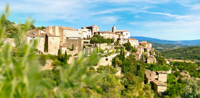 Gordes sits perched in the Luberon region of the French countryside, with green foliage unfocused in the foreground.