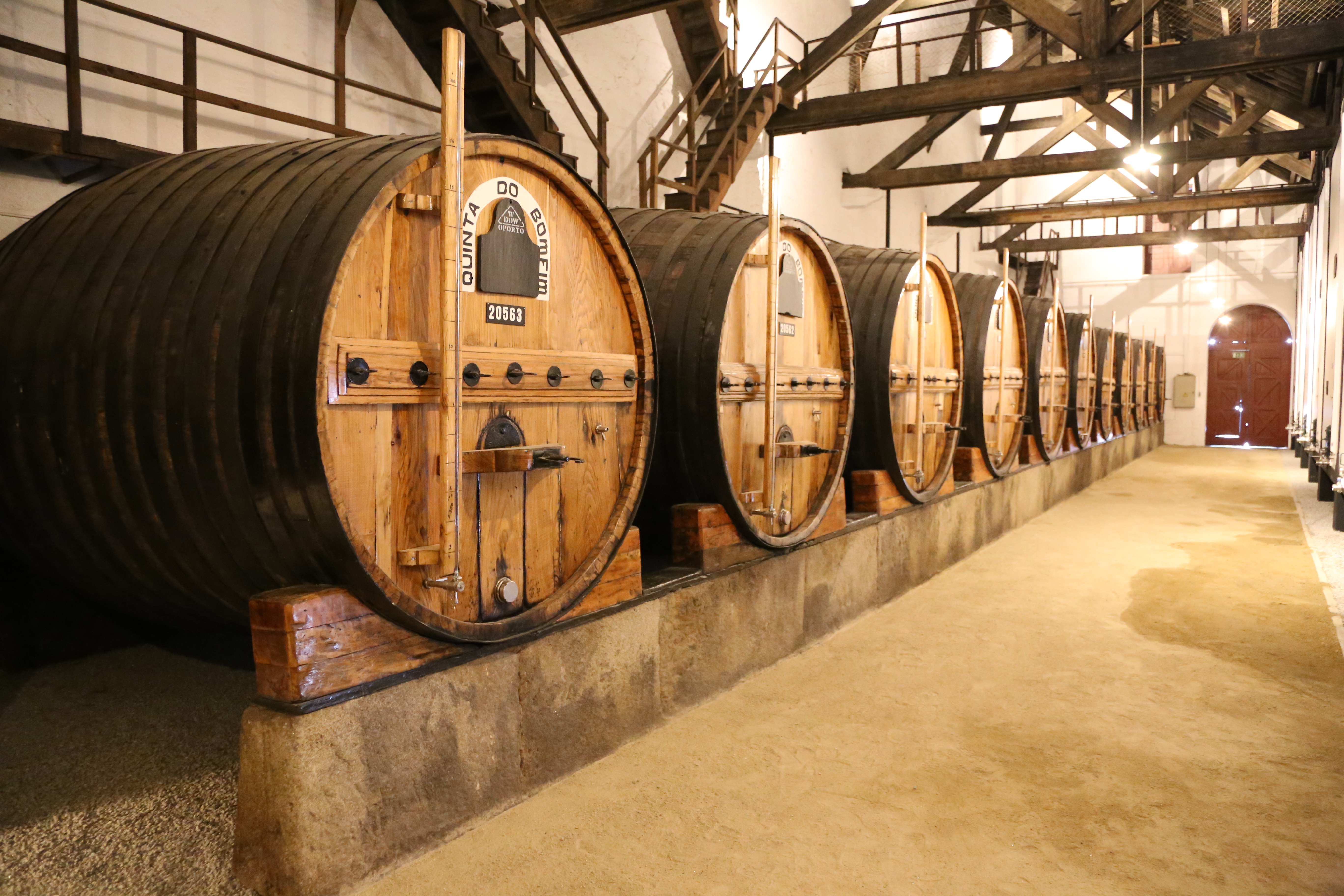 A row of large wooden wine barrels form a row inside a winery or wine estate in Portugal's Douro Valley.