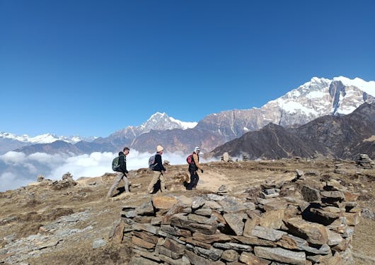 A group of three trekkers along Nepal's Khopra Ridge walk along a plateau with snow capped peaks in the distance.