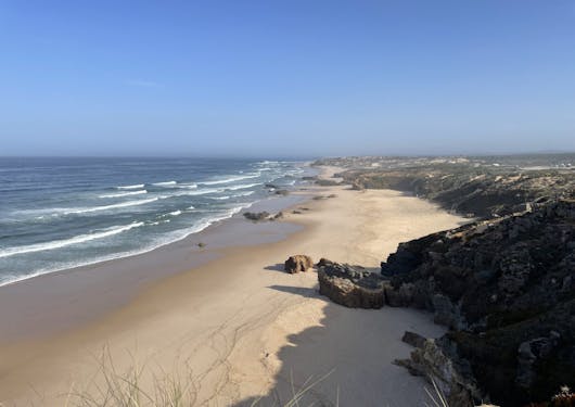 A hike along the Fisherman's Trail in Portugal along the coast of the Atlantic gives views of sandy beaches and gently crashing waves lapping up onto the beach.