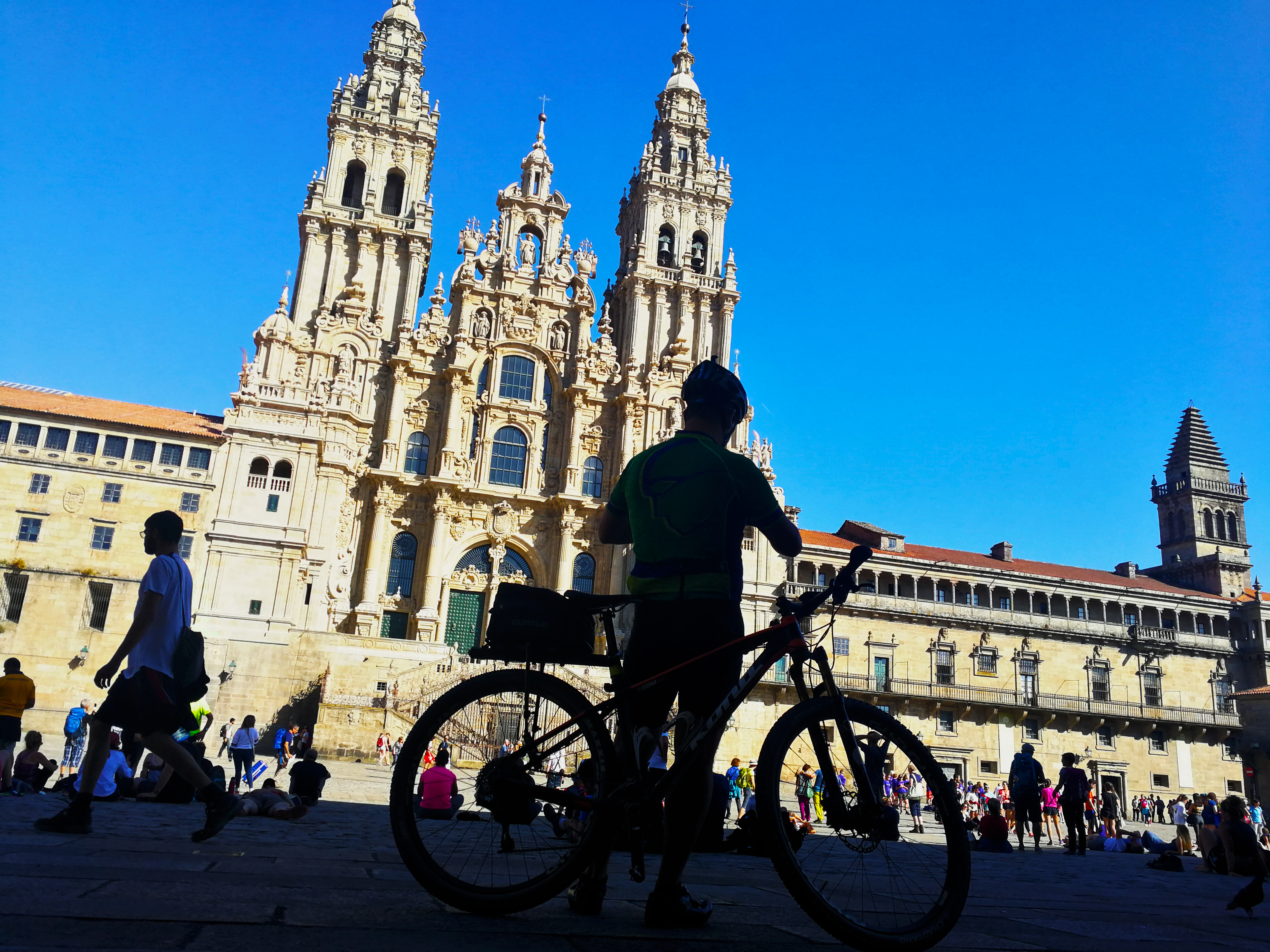 A biker in the shadows stands in front of the majestic Cathedral de Santiago in Spain.