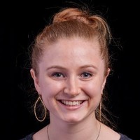 A headshot of a Caucasian woman with reddish-blond hair and gold hoop hearings, smiling broadly.