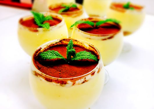 A delectable French custard desert in personal-sized glass cups is shown with a cocoa powder top covering it and a sprig of bright green mint sticking out of the top. This is on a gourmet walking holiday of the southern French alps.