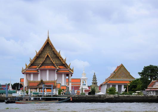 Temples and small structures are seem from the Chao Praya River in Bangkok. The cloud has a light sky cover.