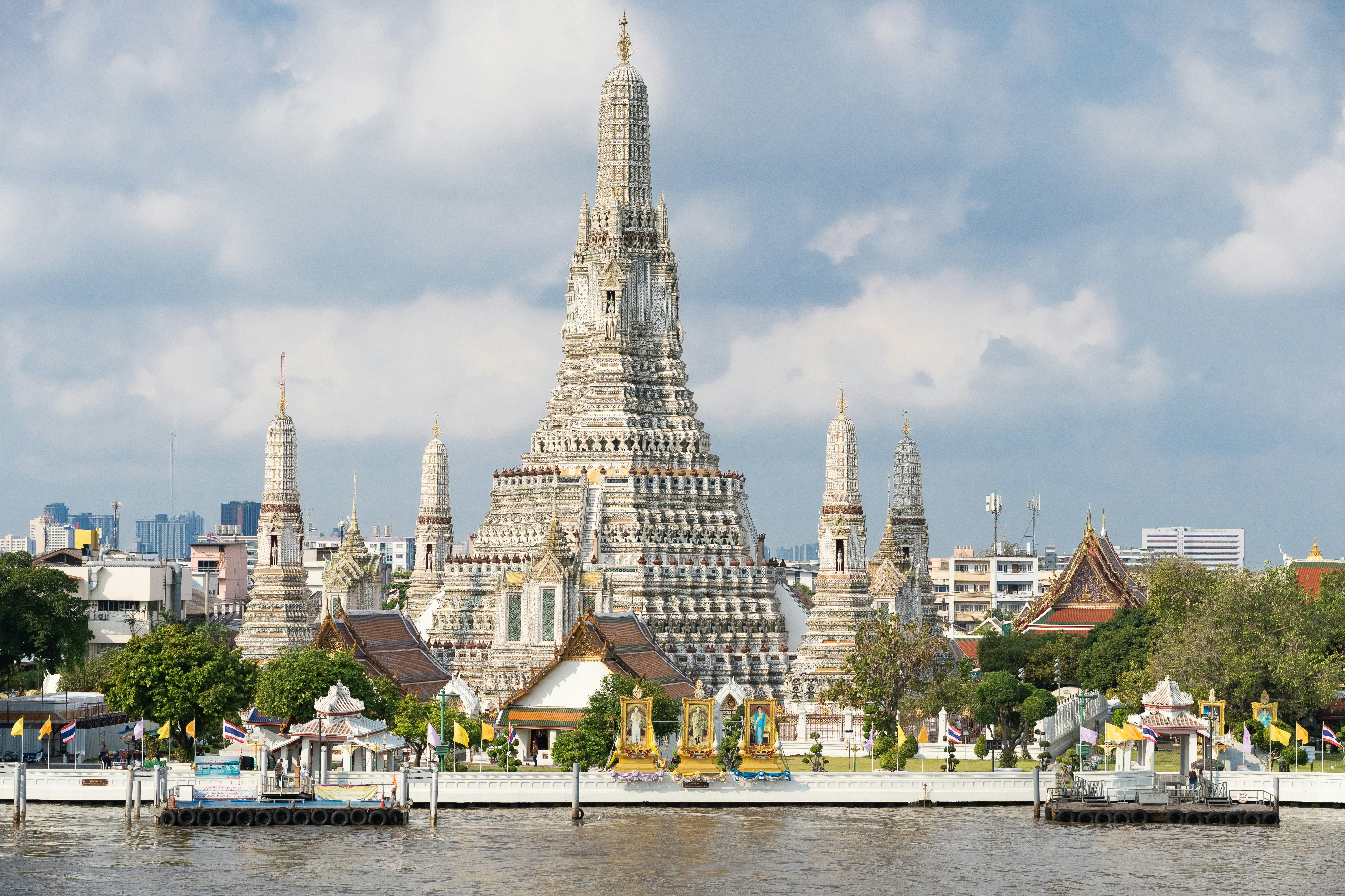 The famous Wat Arun temple is shown in Bangkok with its white stucco and spires in clear view from across the river.