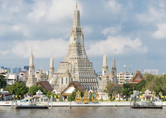 The famous Wat Arun temple is shown in Bangkok with its white stucco and spires in clear view from across the river.