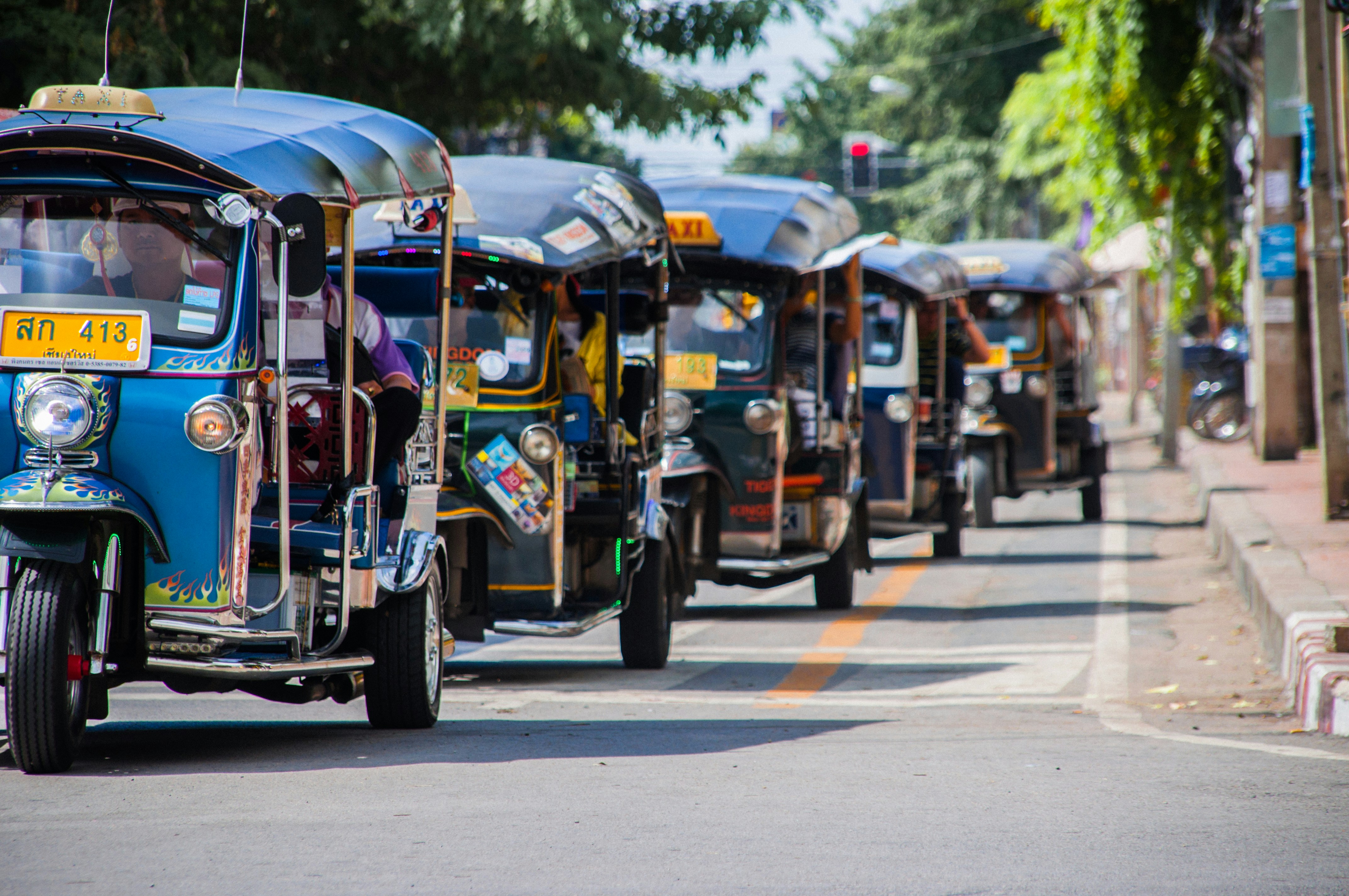 A row of blue tuktuks in Thailand form a line on the pavement waiting to pick up passengers.