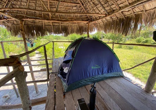 A tent is pitched on a raised wooden platform under a traditional Makuti thatched roof in the Mida Creek Village Community in Kenya.