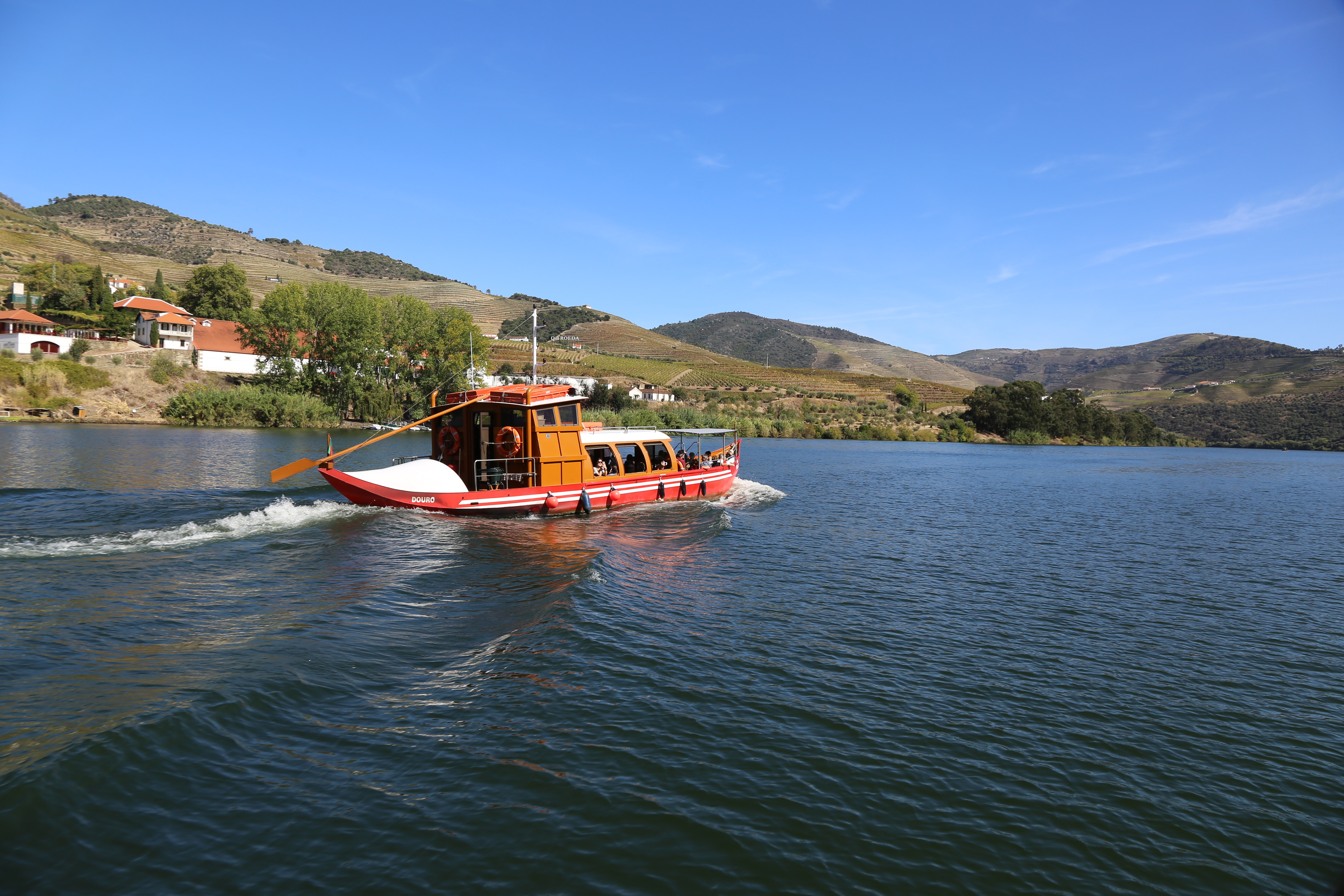 A red and orange passenger boat floats down the Douro River in Portugal.
