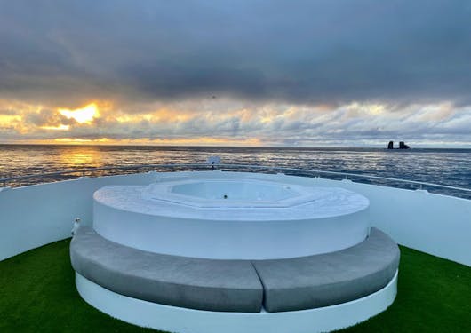 A circular, outdoor seating area with white cushions is shown on the luxury yacht used for the Galapagos Citizen Science scuba diving trip.