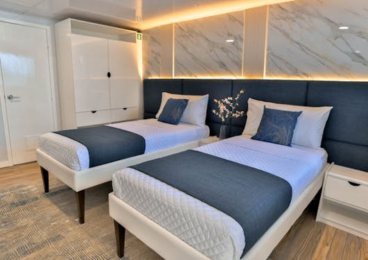 A bedroom with two twin single beds in a shared room is shown on the luxury yacht used for the Galapagos Citizen Science scuba diving trip.