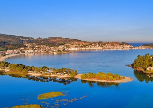 An aerial view of beautiful and varied beaches in Northern Portugal at sunset, with blue water and blue sky and small buildings and trees hugging the coast.