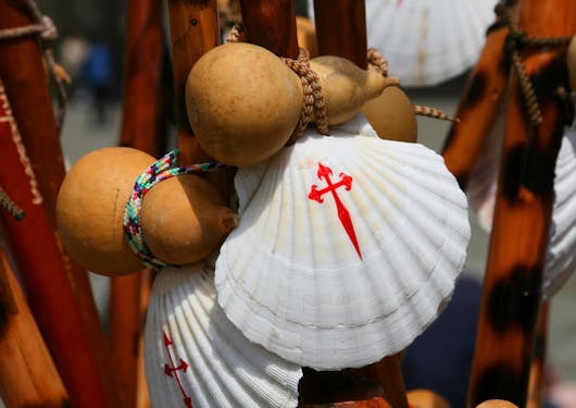 A white scallop shell is shown with a red cross on top of it, it's the classic sign of the Camino de Santiago de Compostela.