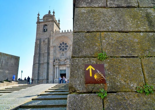 Arrival at the church of Santiago de Compostela in Spain, as seen from the bottom of stairs leading up to the church, with a final brown and yellow Camino marker sign on the right hand side, attached to a wall.