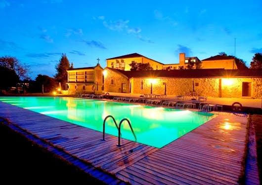 A glowing pool at dusk shows teal green water and a blue sky with the yellow backlit luxury hotel behind the pool. This is in Northern Portugal along the Luxury Coastal Camino trail walk.