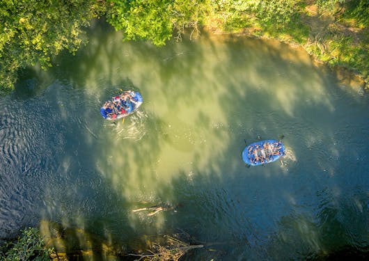 Two inflatable raft boats with travelers on them enjoy a safari boat tour down the river in Costa Rica, surrounded by greenery and as seen from an aerial view above.