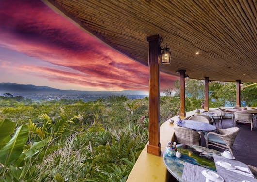 A beautiful, bright pink and red sunset is shown from the windowless, covered dining area of an accommodation in Costa Rica.