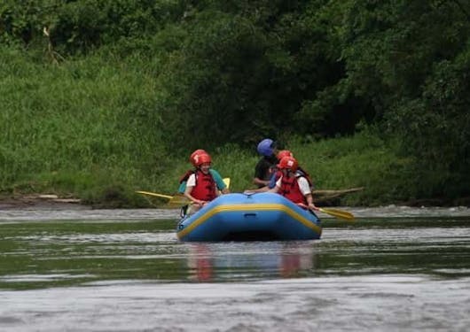 A floating river safari tour shows several people on an inflatable raft lifejackets and helmets as they paddle downstream in Costa Rica.